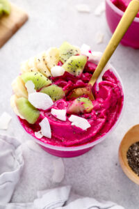 A dragon fruit smoothie bowl topped with banana, kiwi, coconut flakes and chia seeds.